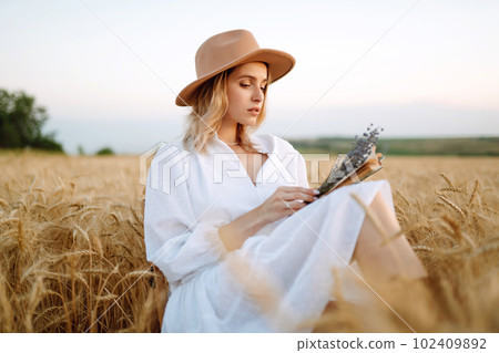 Young woman in white linen dress and hat enjoying a sunny day in a golden wheat field. Summer, beauty. Young woman in white linen dress and hat enjoying a sunny day in a golden wheat field. Summer, beauty. 102409892
