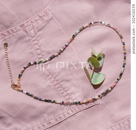 hippie style seed beads necklace. multicolored choker on a pink denim shirt with eucalyptus branch in a pocket. hippie style seed beads necklace. multicolored choker on a pink denim shirt with eucalyptus branch in a pocket. 102410239