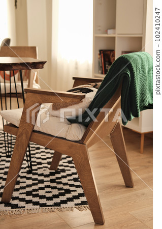 natural wooden armchair midcentury design style, cozy place with green knitted plaid and pillows on armchair.. back view, vertical. natural wooden armchair midcentury design style, cozy place with green knitted plaid and pillows on armchair.. back view, vertical. 102410247