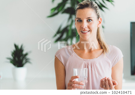 Waist up portrait of smiling blonde woman with blue eyes taking her supplements in the morning 102410471