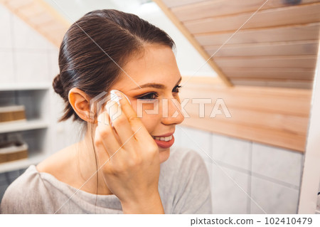 Smiling cheerful young woman cleaning make up off her face late at night in her bathroom Smiling cheerful young woman cleaning make up off her face late at night in her bathroom 102410479