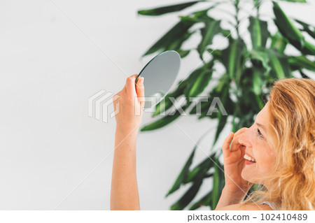Side view of a woman holding a small mirror high up looking at it while doing her makeup Side view of a woman holding a small mirror high up looking at it while doing her makeup 102410489