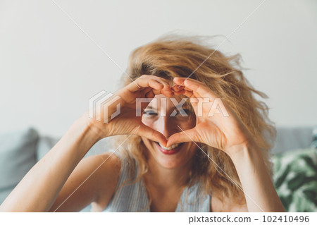 Waist up portrait woman holding hand in heart shape in front of her face  102410496
