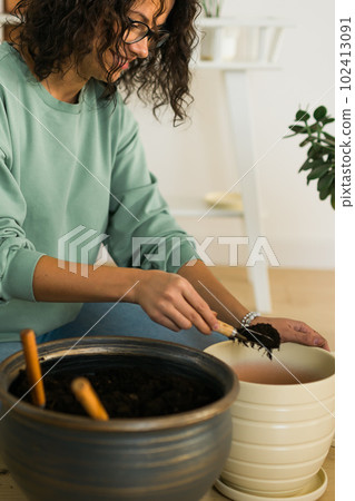 Woman grows potted plants at home watering and take care flowers - gardening and houseplant care concept 102413091