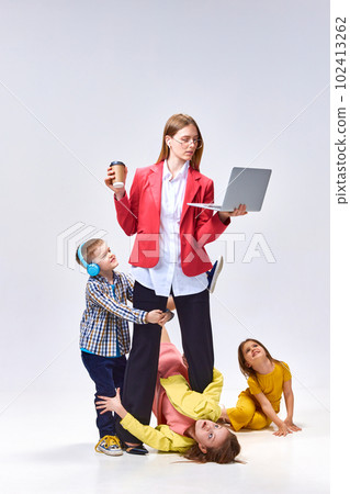 Portrait of businesswoman with laptop and little children playing around her with noise against grey studio background 102413262