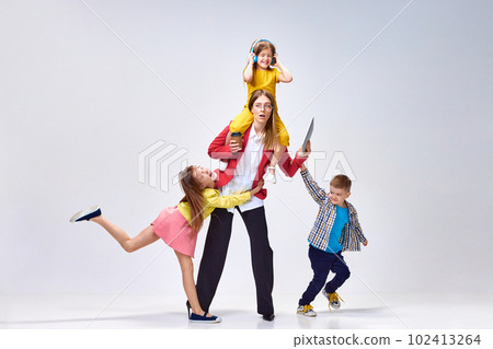 Work and parenting. Portrait woman with tablet and coffee and playful, noisy little kids posing against grey studio background Work and parenting. Portrait woman with tablet and coffee and playful, noisy little kids posing against grey studio background 102413264