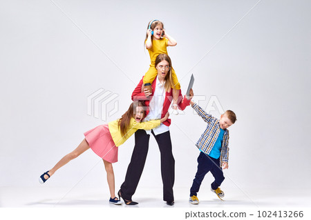 Multitasking. Work and parenting. Portrait woman and playful, noisy little kids posing against grey studio background Multitasking. Work and parenting. Portrait woman and playful, noisy little kids posing against grey studio background 102413266