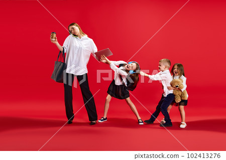 Portrait of busy woman talking on phone, working, little playful kids disturbing her against red studio background. Work and school Portrait of busy woman talking on phone, working, little playful kids disturbing her against red studio background. Work and school 102413276