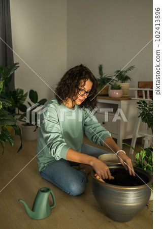 Woman grows potted plants at home watering and take care flowers - gardening and houseplant care concept Woman grows potted plants at home watering and take care flowers - gardening and houseplant care concept 102413896