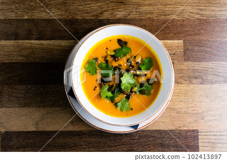 Pumpkin cream soup with parsley on gray stone and wooden background. Top view, copy space Pumpkin cream soup with parsley on gray stone and wooden background. Top view, copy space 102413897