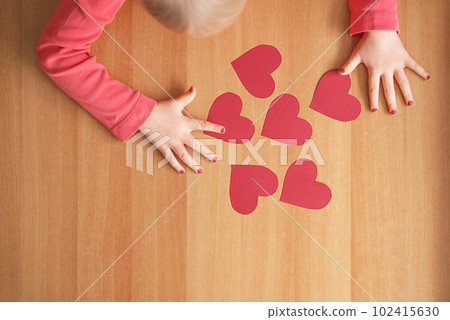 A child crafting hearts from red paper. Background for valentines day or mothers day. A child crafting hearts from red paper. Background for valentines day or mothers day. 102415630