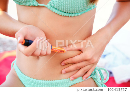 A teenage girl injects herself with insulin in her stomach on the beach. Diabetic lifestyle. A teenage girl injects herself with insulin in her stomach on the beach. Diabetic lifestyle. 102415757