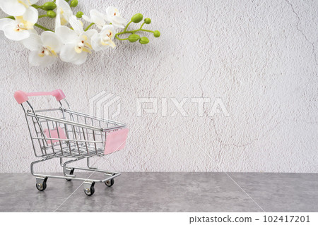 The empty toy metal supermarket shopping cart on old cement background with white orchid flower. 102417201