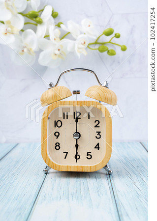 The Wooden alarm clock on wooden floor with white orchid flower. The Wooden alarm clock on wooden floor with white orchid flower. 102417254