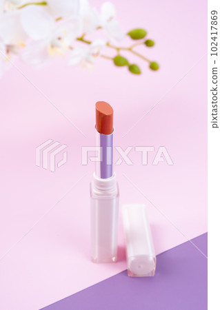 A Red color beautiful lipstick with white orchid flower on pink and purple background. 102417869