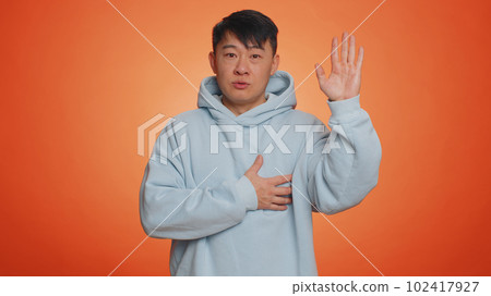 Asian man raising hand to take oath, promising to be honest and to tell truth, keeping hand on chest 102417927