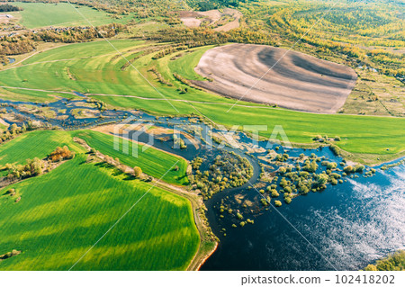 Aerial View Green meadows And River Landscape In Sunny Spring Summer Day. Top View Of Nature, Bird's Eye View. Trees Standing In Water During Spring Flood floodwaters. woods in Water deluge During A Aerial View Green meadows And River Landscape In Sunny Spring Summer Day. Top View Of Nature, Bird's Eye View. Trees Standing In Water During Spring Flood floodwaters. woods in Water deluge During A 102418202