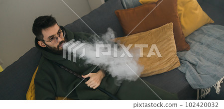 Banner bearded millennial or gen z man smoking hookah while relaxing on sofa at home copy space - chill time and resting concept Banner bearded millennial or gen z man smoking hookah while relaxing on sofa at home copy space - chill time and resting concept 102420032