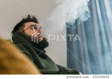 Bearded man is smoking hookah at home and blowing cloud of smoke - chill time and resting concept Bearded man is smoking hookah at home and blowing cloud of smoke - chill time and resting concept 102420050
