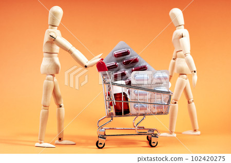 Dummy pushing a shopping trolley with medicines on an orange background. Medicine concept Dummy pushing a shopping trolley with medicines on an orange background. Medicine concept 102420275