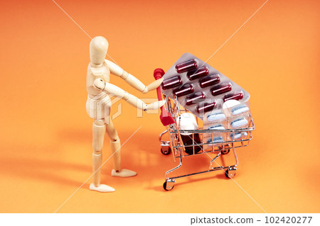 Dummy pushing a shopping trolley with medicines on an orange background. Medicine concept Dummy pushing a shopping trolley with medicines on an orange background. Medicine concept 102420277