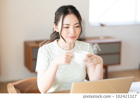 A young woman looking at a computer while drinking coffee A young woman looking at a computer while drinking coffee 102421327
