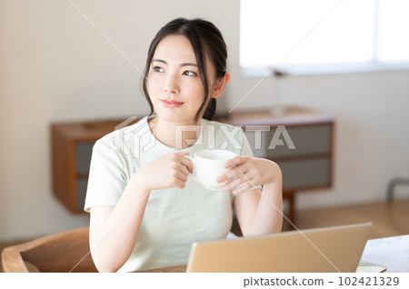 A young woman looking at a computer while drinking coffee A young woman looking at a computer while drinking coffee 102421329
