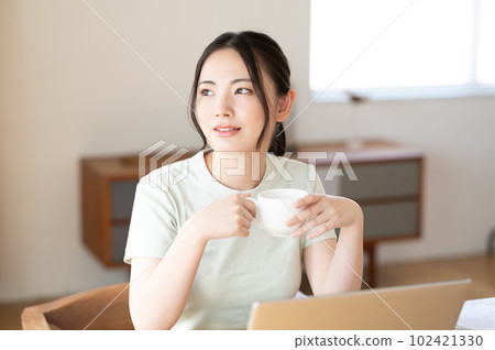 A young woman looking at a computer while drinking coffee A young woman looking at a computer while drinking coffee 102421330