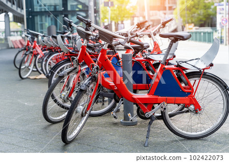 Closeup view many red city bikes parked in row at german Hamburg city street rental parking sharing station or sale. Healthy ecology urban transportation. Sport environmental transport infrastructure Closeup view many red city bikes parked in row at german Hamburg city street rental parking sharing station or sale. Healthy ecology urban transportation. Sport environmental transport infrastructure 102422073