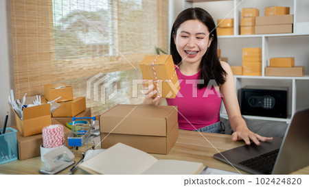 Woman uses a laptop to chat with customers who come to order product, Freelance work at home, Packaging on background, Sell online, Small business owner, Online shopping SME entrepreneur. Woman uses a laptop to chat with customers who come to order product, Freelance work at home, Packaging on background, Sell online, Small business owner, Online shopping SME entrepreneur. 102424820