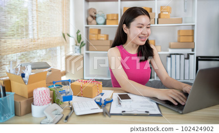 Woman uses a laptop to chat with customers who come to order product, Freelance work at home, Packaging on background, Sell online, Small business owner, Online shopping SME entrepreneur. Woman uses a laptop to chat with customers who come to order product, Freelance work at home, Packaging on background, Sell online, Small business owner, Online shopping SME entrepreneur. 102424902