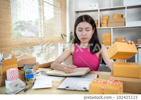Woman is writing down the customer's details and addresses on the notebook or post box in order to prepare for shipping according to the information, Packing box, Sell online, Freelance working. 102425115