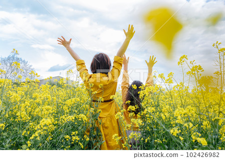 back view of mother and daughter standing with arms up in the field with yellow flowers back view of mother and daughter standing with arms up in the field with yellow flowers 102426982