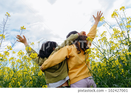 back view of two children hugging each other in the field with yellow flowers 102427001