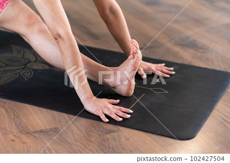 Professional yoga exercise for flexible body woman stretching legs on black mat put on parquet in modern studio sportive lady enjoying favorite hobby after work closeup 102427504