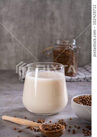 Vegan dairy-free buckwheat milk in a glass and cereals in a bowl on the table vertical view Vegan dairy-free buckwheat milk in a glass and cereals in a bowl on the table vertical view 102428712