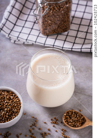 Lactose free dietary buckwheat milk in a glass and seeds in a bowl on the table vertical view 102428713
