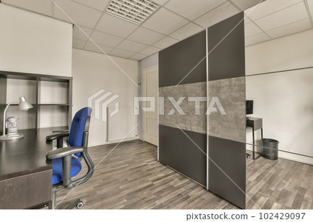 an office space with wood flooring and white walls, there is a blue chair in front of the wall an office space with wood flooring and white walls, there is a blue chair in front of the wall 102429097