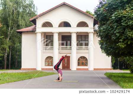 Full length side view of young strong sporty woman doing yoga asana supported headstand on the street, Salamba Sirsasana, complex balanced posture for a healthy body and spirit. 102429174