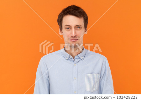 Portrait of unhappy sad depressed man standing looking at camera, being in bad mood, expressing sadness and sorrow, wearing light blue shirt. Indoor studio shot isolated on orange background. 102429222