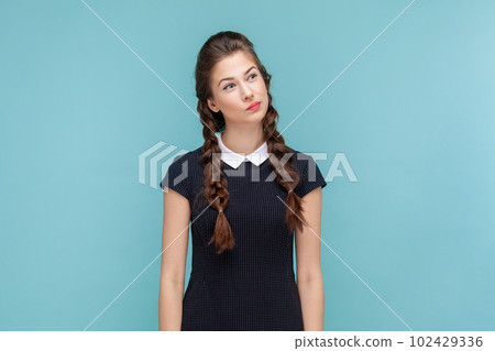Portrait of pensive thoughtful woman with braids standing and looking away, making decision, thinks about solving problem, wearing black dress. woman Indoor studio shot isolated on blue background. 102429336