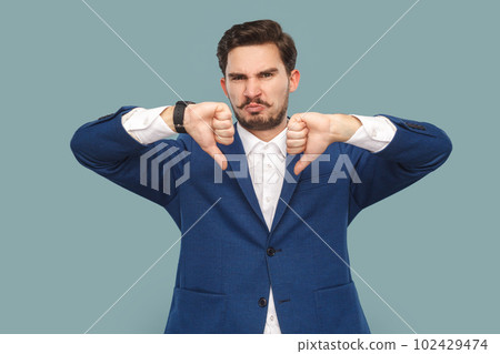 Portrait of sad displeased handsome man with mustache standing and showing dislike gesture, disagree, wearing official style suit. Indoor studio shot isolated on light blue background. 102429474