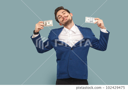 Portrait of happy smiling delighted man with mustache standing with dollar banknotes and looking at camera with pride, wearing official style suit. Indoor studio shot isolated on light blue background 102429475