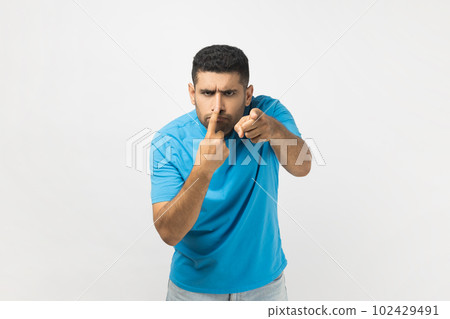 Portrait of funny unshaven man wearing blue T- shirt standing touching his nose with finger and showing lie gesture, body language. Indoor studio shot isolated on gray background. 102429491