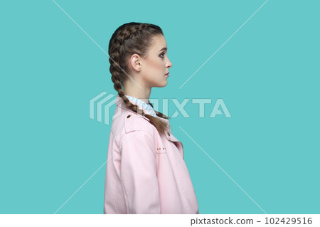 Side view portrait of strict bossy young teenager girl with braids wearing pink jacket looking ahead with serious facial expression, being in bad mood. Indoor studio shot isolated on green background. 102429516