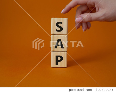 SAP - Systems Applications Products. Wooden cubes with word SAP. Businessman hand. Beautiful orange background. Business and System Application Product concept. Copy space. 102429923