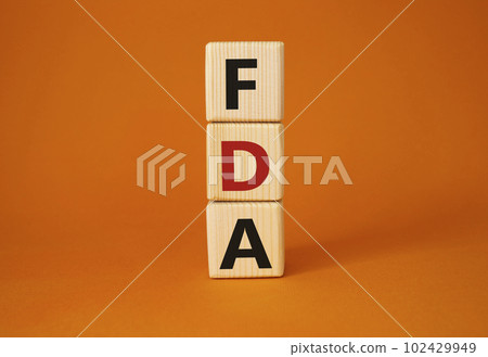 FDA - Food Drug Administration symbol. Wooden cubes with word FDA. Beautiful orange background. Medical and Food Drug Administration concept. Copy space. 102429949
