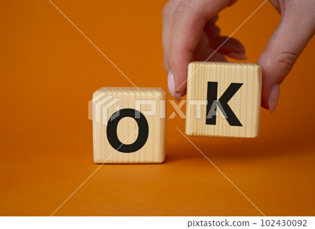 Ok symbol. Concept word Ok on wooden cubes. Businessman hand. Beautiful orange background. Business and Ok concept. Copy space. Ok symbol. Concept word Ok on wooden cubes. Businessman hand. Beautiful orange background. Business and Ok concept. Copy space. 102430092
