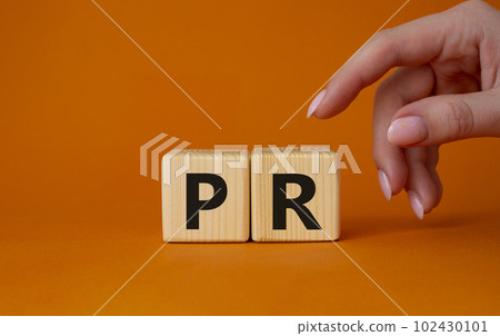 PR - Public Relations symbol. Concept word PR on wooden cubes. Businessman hand. Beautiful orange background. Business and PR concept. Copy space. PR - Public Relations symbol. Concept word PR on wooden cubes. Businessman hand. Beautiful orange background. Business and PR concept. Copy space. 102430101