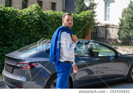 Attractive bearded man in a blue suit near a black car in the countryside in summer. 102430842
